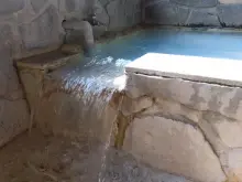 alt=”ホワイトブルーのお湯が溢れる岩風呂"